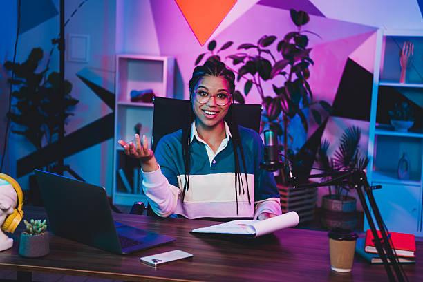 istock Casual female podcaster with laptop and microphone in vibrant neon studio, engaging with audience during live broadcast 2235752812