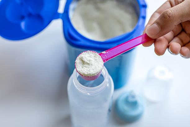 Unrecognisable mother pouring baby food formula into a bottle and preparing baby food