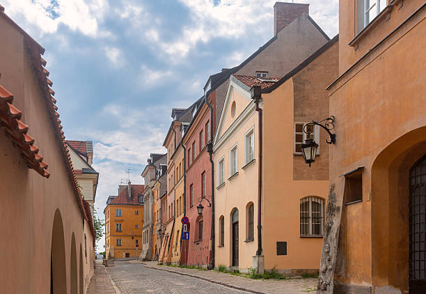Historic cobblestone street in Old Town, Warsaw, Poland, lined with colorful residential buildings under a cloudy sky