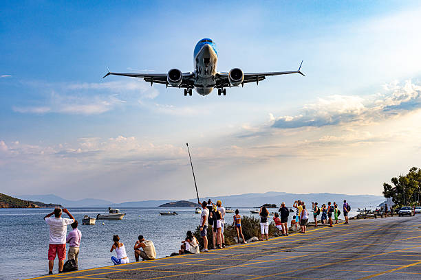 Skiathos, Greece – 5 September 2025: A passenger plane approaches for landing at Skiathos Alexandros Papadiamantis Airport, flying extremely low over tourists gathered near the runway. Known as one of the most dangerous airports in Europe, Skiathos has become famous among aviation enthusiasts for its short runway and dramatic landings.