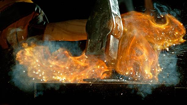 The blacksmith manually forging the molten metal on the anvil in smithy with spark fireworks. Action shot, cinematic and dramatic lights. Freeze motion.