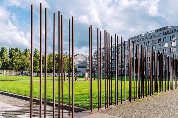 Capturing the iconic Berlin Wall Memorial with its steel pillars symbolizing history and cultural significance, set along Bernauer Strasse, surrounded by a modern urban landscape and green open spaces.