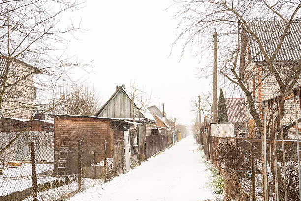 Snowy rural alleyway with rustic wooden sheds and bare winter trees.