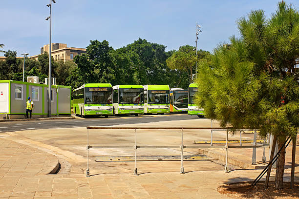 Valletta, Malta - 09/03/2025: Modern green city buses parked at a bus station surrounded by trees under clear sky.