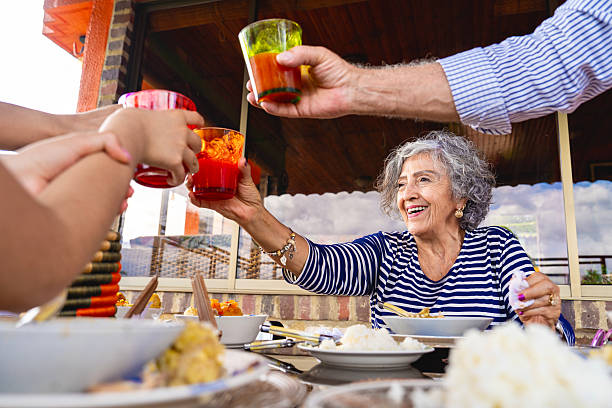Smiling senior woman toasting with her multigenerational family while having lunch outdoors, celebrating togetherness and a joyful family lifestyle.