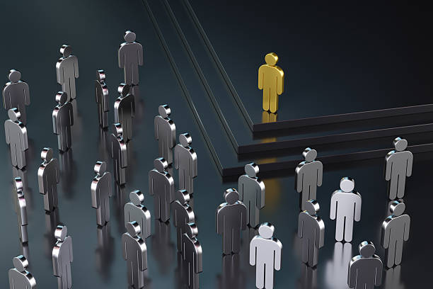 A crowd of wooden mannequins stands together on a reflective surface, with one mannequin uniquely painted with colour, drawing focus to its distinctiveness amidst the group. The lighting highlights themes of individuality and uniqueness. CGI