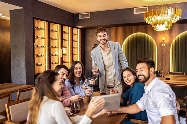 istock Group of young friends sitting in modern cafe using tablet for video call, connecting with someone remotely. 2235768679