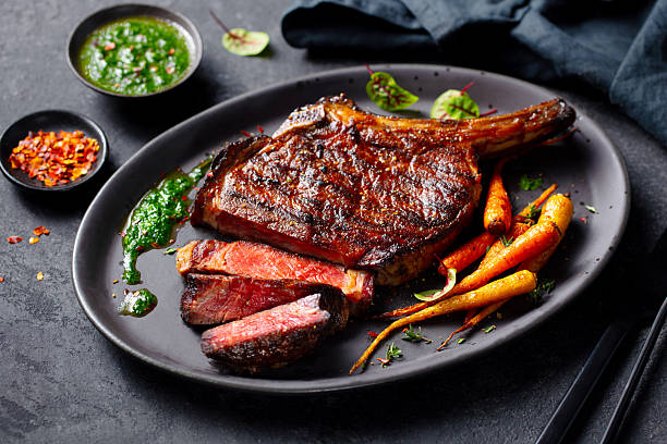 istock Tomahawk steak with chimichurri sauce on a black plate. Grey background. Close up. 2235770025