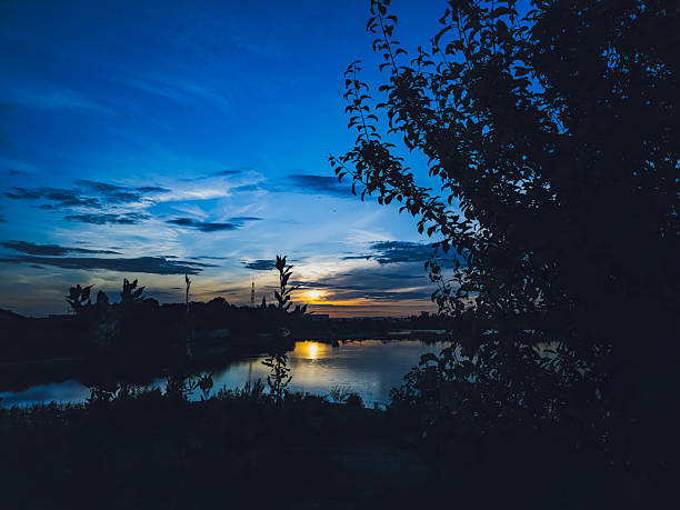 Dramatic sunset sky over a calm lake in Baden-Baden, Germany. Vibrant blue hour colors with warm sunlight reflecting on the water, framed by dark tree silhouettes. Scenic evening landscape perfect for travel, nature and atmospheric background themes.