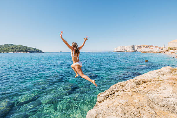 istock Woman Jumping from Rocky Cliff into Sea 2235775626
