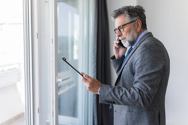 istock Businessman talking on phone and reading documents near window in office 2235778275