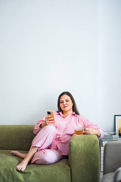 istock Woman Relaxing on Sofa While Using Smartphone and Enjoying a Cup of Tea 2235780793
