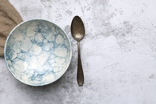Flat lay of two artisanal ceramic bowls with a rustic spoon placed on a light stone surface. Minimalist composition perfect for kitchenware advertising or interior design.