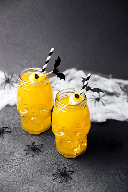istock Two skull jars hold orange Halloween drinks with eyeball garnishes, bats and spooky spiders. 2235784778