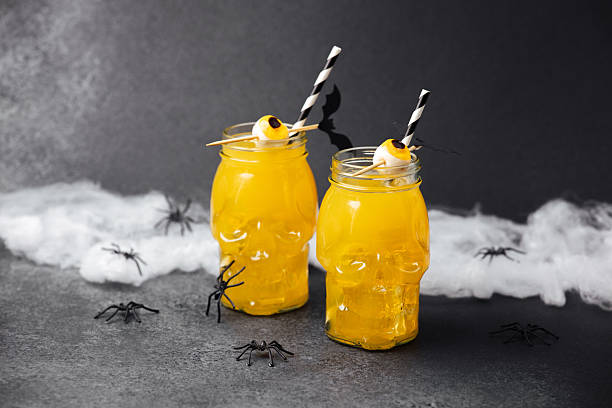 istock Two skull jars with yellow drinks, spooky decorations, spiderwebs, and spiders on dark stone background. 2235784781