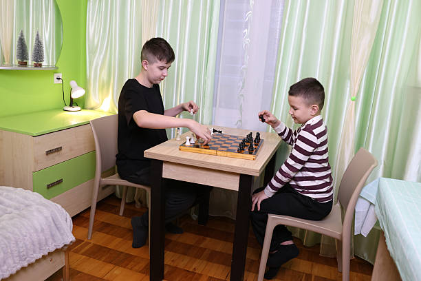 Boys playing chess while sitting at the table in the room. Board game concept