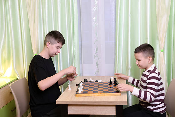 istock Boys playing chess while sitting at the table in the room. Board game concept 2235788195