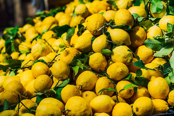 A vibrant display of fresh and ripe lemons with green leaves in a Sicilian market, emphasizing the bright yellow hues and freshness of the fruit.