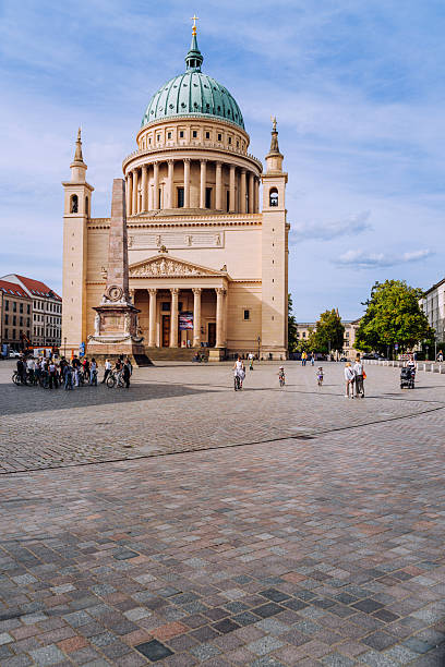 Beautiful cathedral with a copper dome, surrounded by a lively square, captured under a clear sky in Potsdam, Germany.