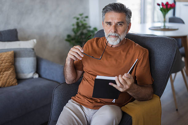 Portrait of a mature man relaxing on an armchair, reading a book and holding his eyeglasses