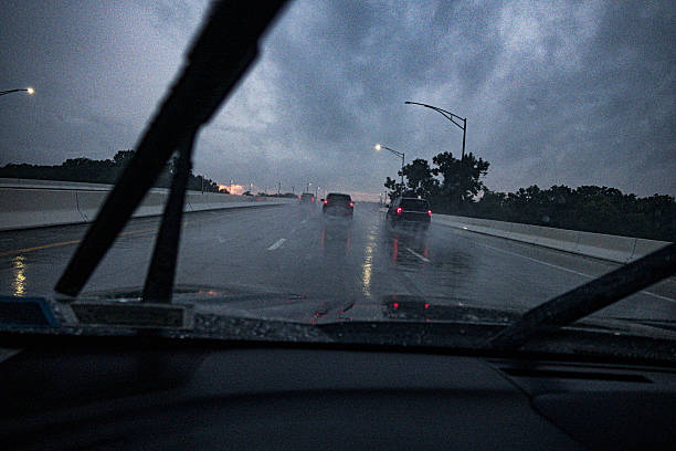 Windshield wipers slashing and splashing back and forth rapidly on a car speeding along an expressway highway just after dusk during a rain storm downpour.