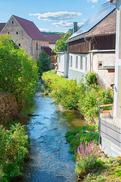Small town of Kastl, Bavaria, Germany. Charming scenery showcasing a clear stream flowing among traditional buildings surrounded by greenery, ideal for themes of tranquility, nature, and countryside living.