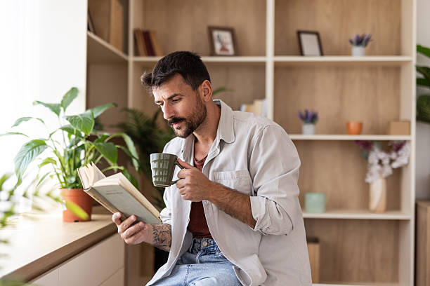 istock Young man reading a book and drinking coffee at home 2235797208