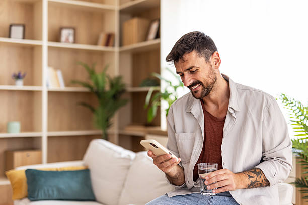 istock Smiling man using smartphone and drinking water at home 2235798723