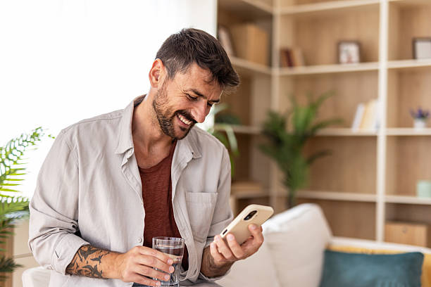 istock Smiling man using smartphone and drinking water at home 2235798768