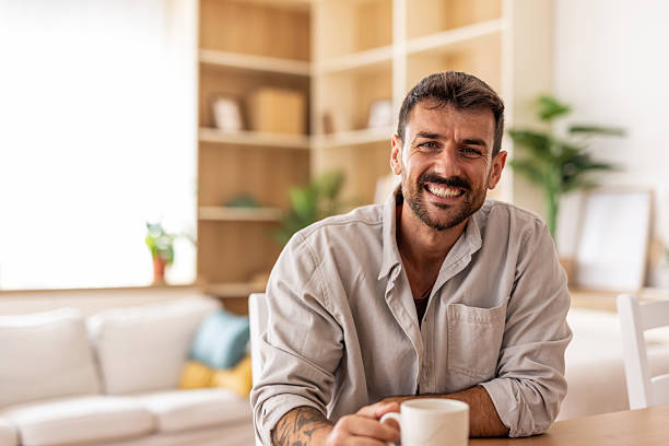 istock Smiling man sitting at table drinking coffee at home 2235799174
