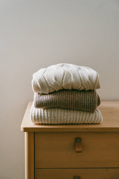 istock Stack of folded warm knitted sweaters in beige, brown and white tones placed on a dresser. Cozy autumn and winter mood. 2235804723
