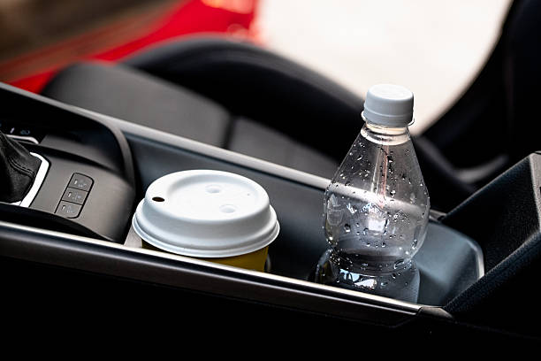 A disposable coffee cup and a plastic water bottle placed side by side in a car's cup holders. A minimalistic depiction of on-the-go lifestyle, hydration, caffeine habits and the environmental conversation around single-use packaging in daily life.