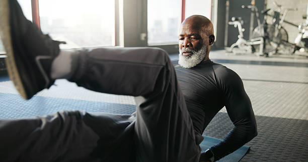 istock Legs, exercise and mature black man in gym for core strength, workout and training on floor. Sports center, serious and person on fitness mat for wellness, health and stretching muscles for mobility 2235811395