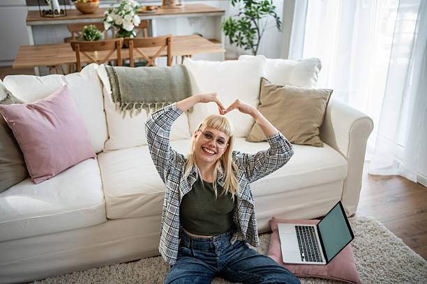 istock Happy young woman making heart shape with hands while using laptop at home 2235817009