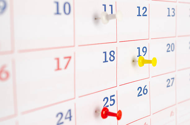 Red, yellow and white thumbtacks on a calendar page. Business concept.