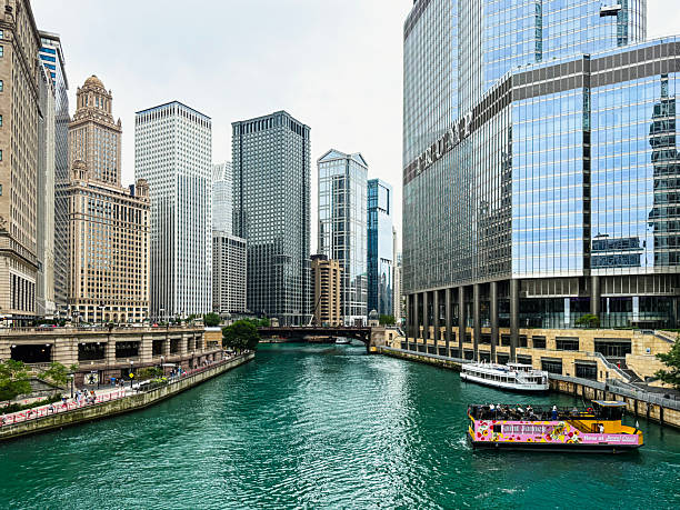 Vertical view of the Chicago River lined with modern skyscrapers and boats sailing through the water on a sunny day in Illinois, USA.