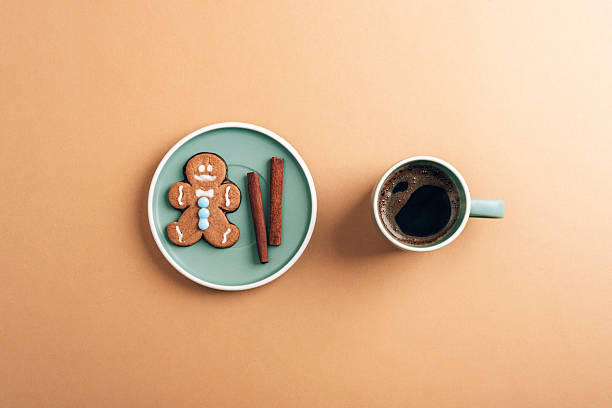 Flat lay of a gingerbread cookie with cinnamon sticks and coffee on a minimalistic beige table. Top view, flat lay.