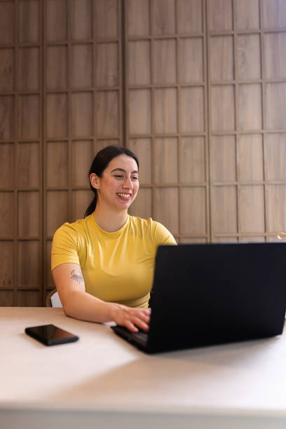 istock Smiling woman working on laptop at modern workspace during daylight while sitting at wooden table with smartphone nearby 2235827138