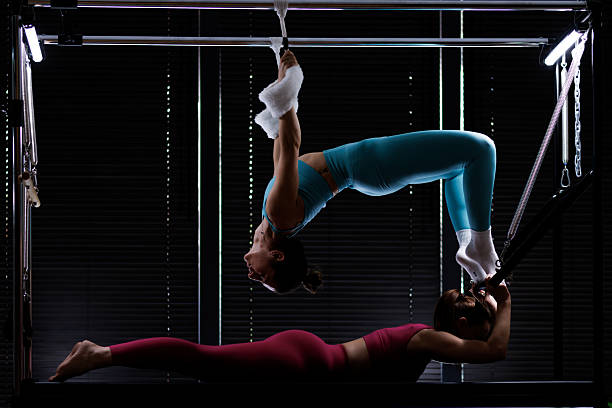 istock Two women practice aerial acrobatics on a reformer in a dimly lit studio, showcasing strength and balance during an evening training session 2235827559