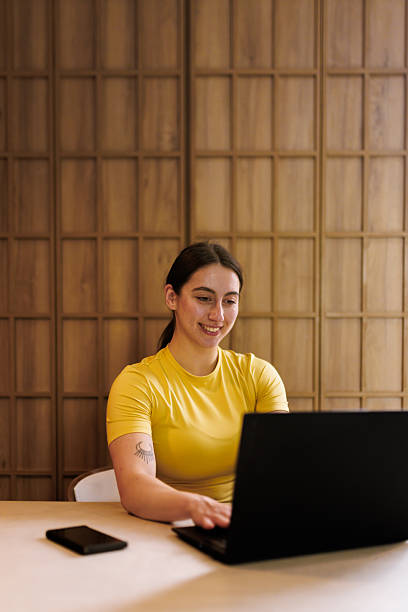 istock Woman sitting at desk using laptop in modern workspace during daytime, focused on her tasks, surrounded by warm wooden decor 2235827645