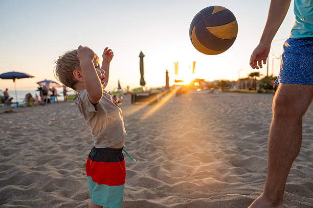 Happy little boy having fun playing with dad on the beach, they are playing with ball together