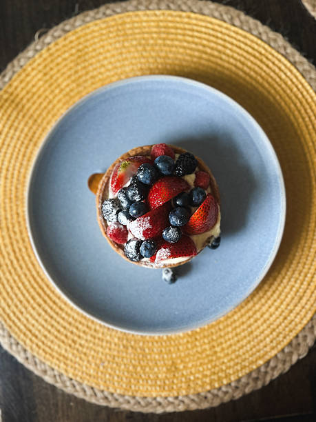 Delicious fruit tart with fresh berries and powdered sugar on a blue plate
