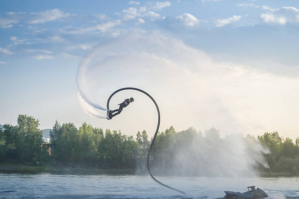A skilled individual performs an impressive flyboard stunt, soaring above the water with a graceful curve. The backdrop features lush green trees and a serene lake.