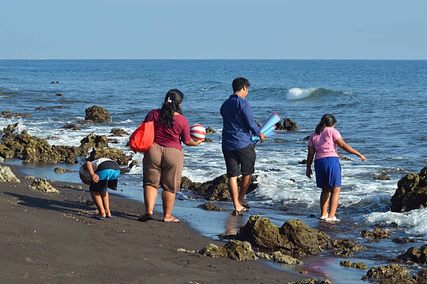istock Young boy picking item from sand while family walks nearby 2235847329