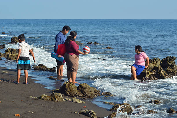 istock Daughter sitting on rock while family observes foamy waves 2235847345