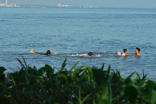 The mother and daughter float and swim together in shallow seawater as the family enjoys playful relaxation in the calm coastal waves.