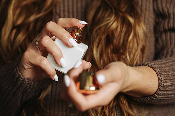 Woman spraying perfume from white bottle on wrist. Elegant female hands with manicure using fragrance.
