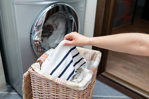 istock Woman's hand taking clothes from wicker basket to washing machine 2235851058