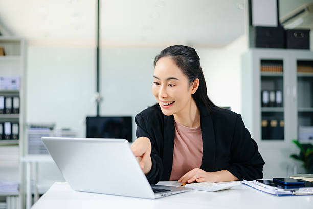 istock Confident Asian businesswoman using tablet in modern office with laptop and documents, showcasing finance, remote work 2235851944