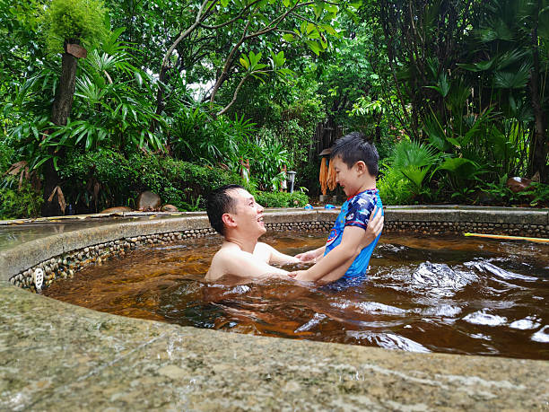 The cheerful father lifted his son up from the hot spring pool